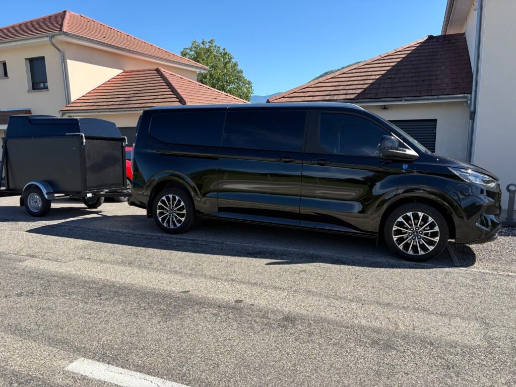 Van VTC noir avec remorque porte-bagages garé devant une maison